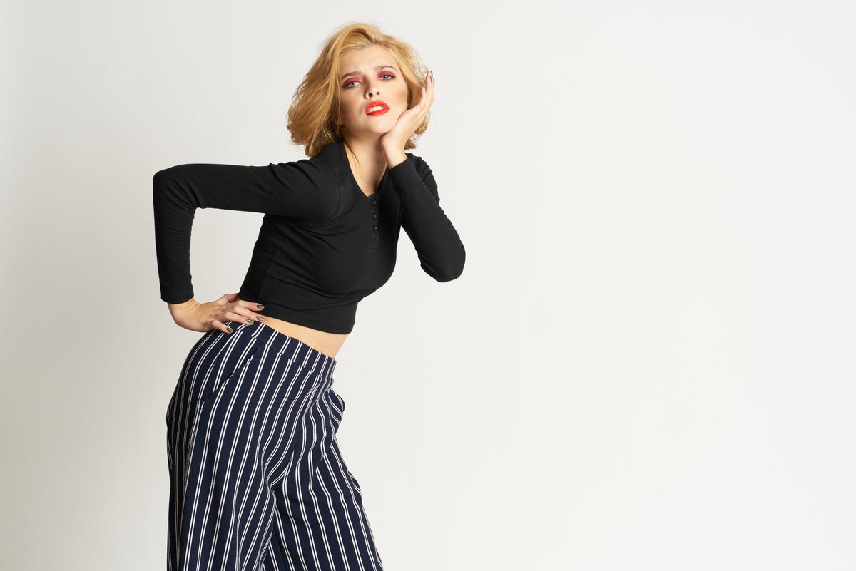 Pretty Woman in Black Sweater Striped Pants Fashion Clothes Light Background Studio